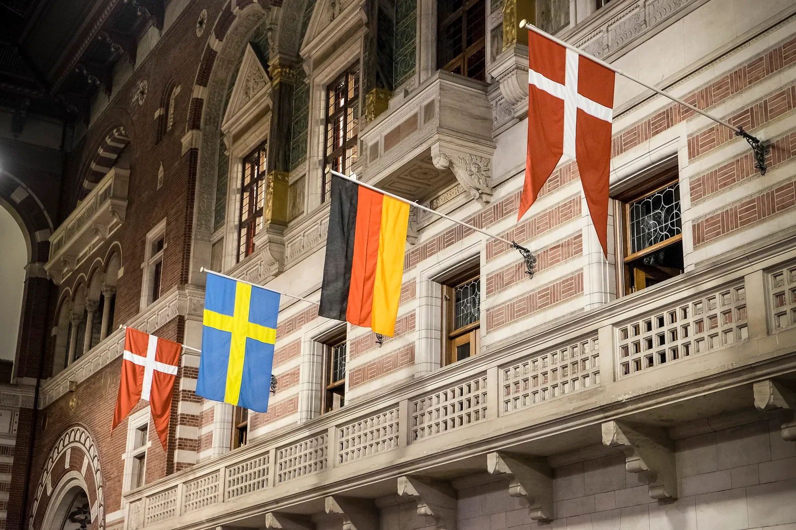 Danske, svenske og tyske flag på stænger ud fra en rødstribet facade