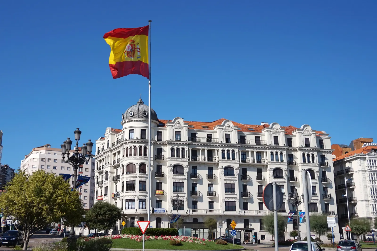Un alto mástil con una gran bandera de España ante un edificio blanco de Santander