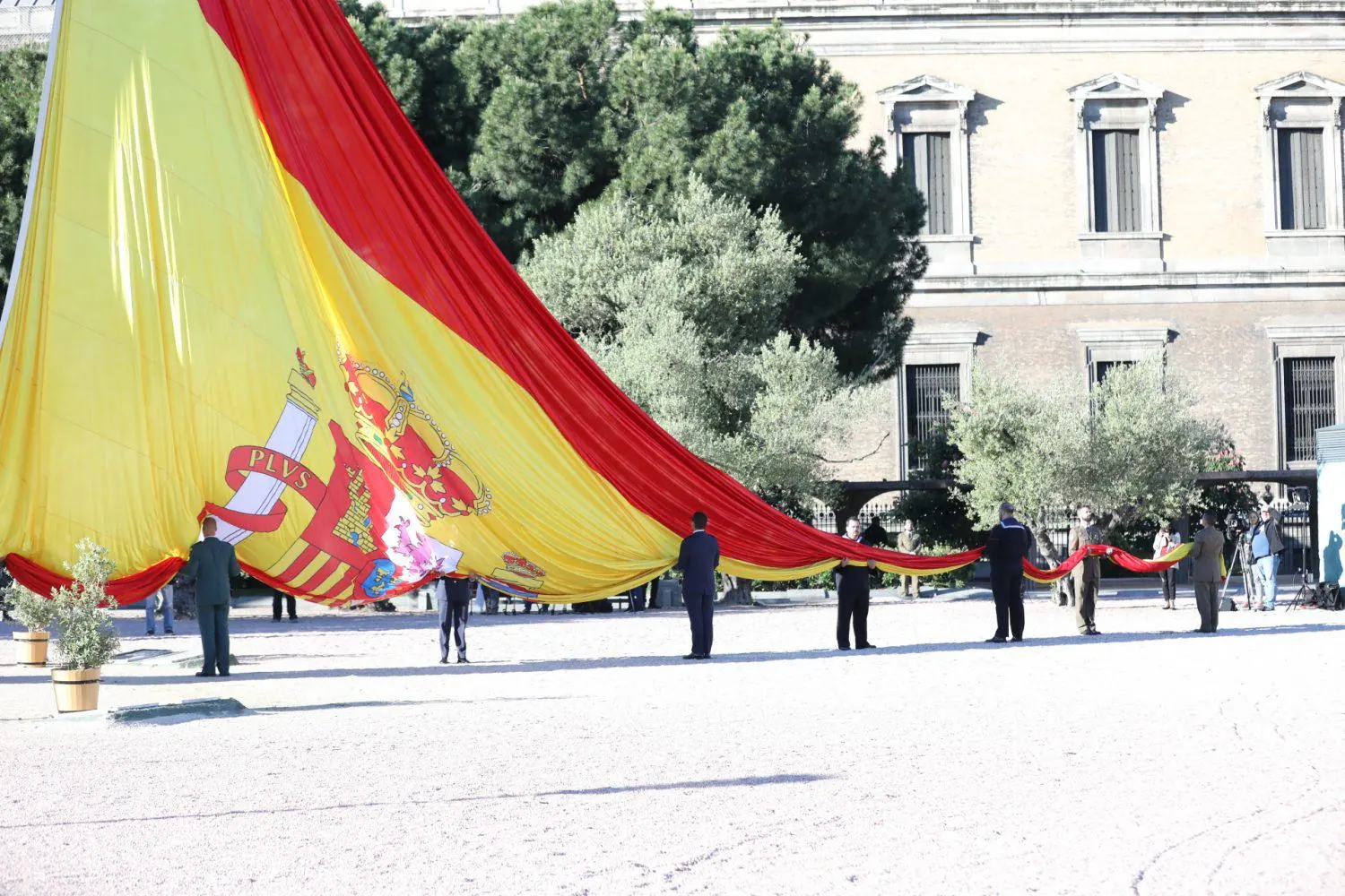 Un grupo de personas sostiene la gran bandera de España en la plaza de Colón de Madrid durante el izado por San Isidro
