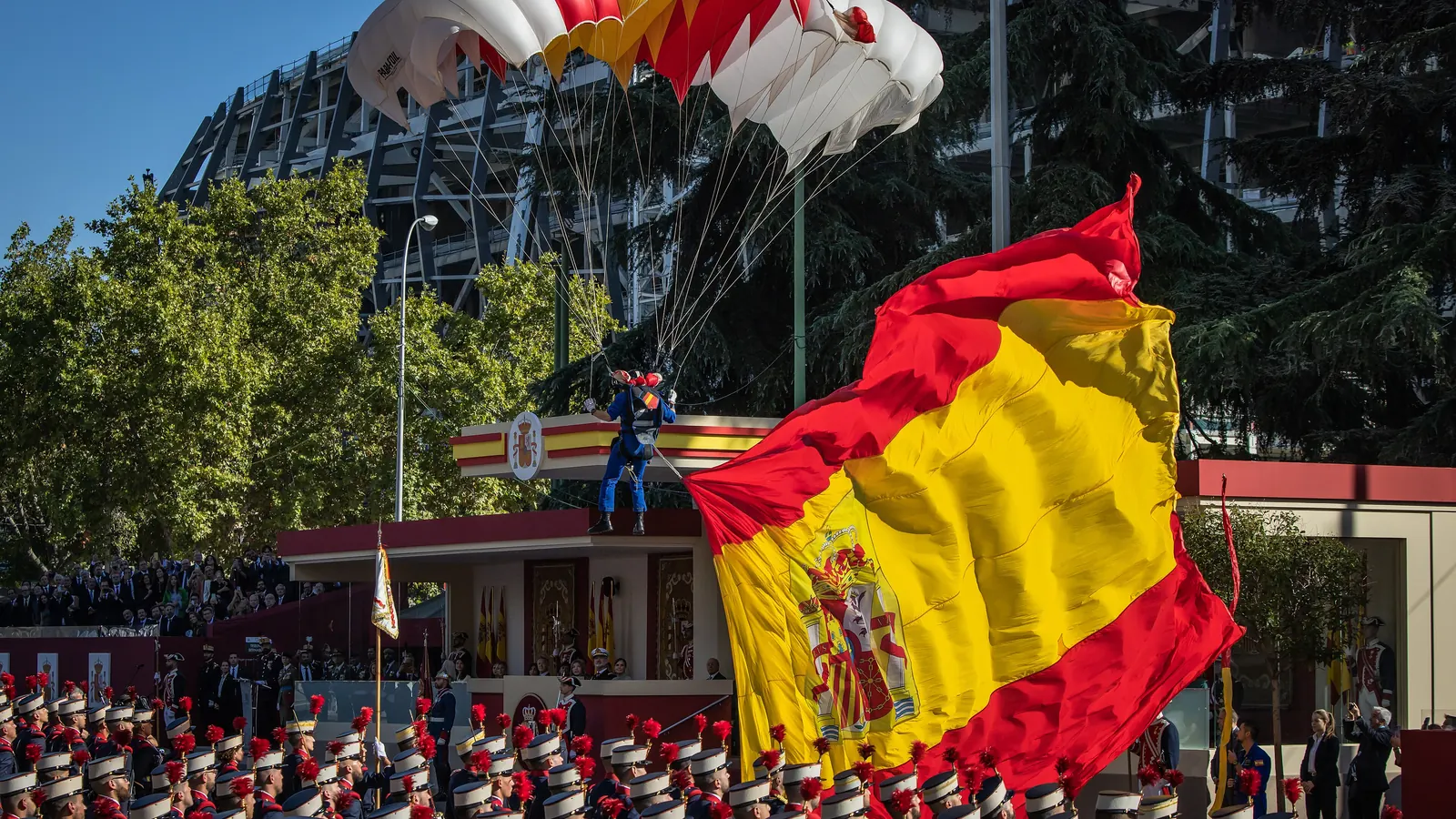 Un paracaidista desciende con una gran bandera de España sobre la tribuna del desfile del 12 de octubre de 2022 en Madrid
