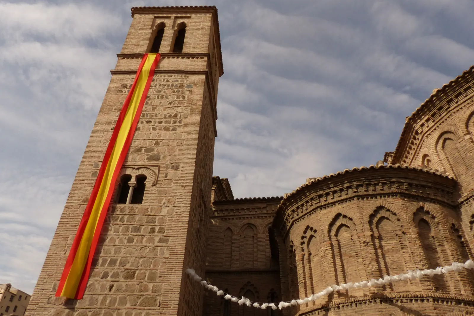 Una larga bandera de España cuelga de la torre mudéjar de Santiago del Arrabal, en Toledo
