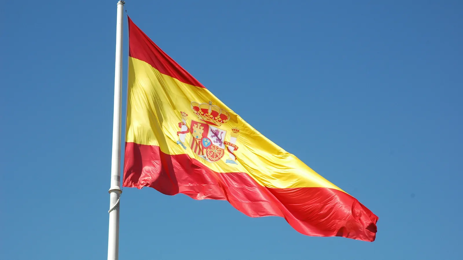 La gran bandera de España ondea en lo alto del mástil de la plaza de Colón de Madrid, sobre un cielo azul