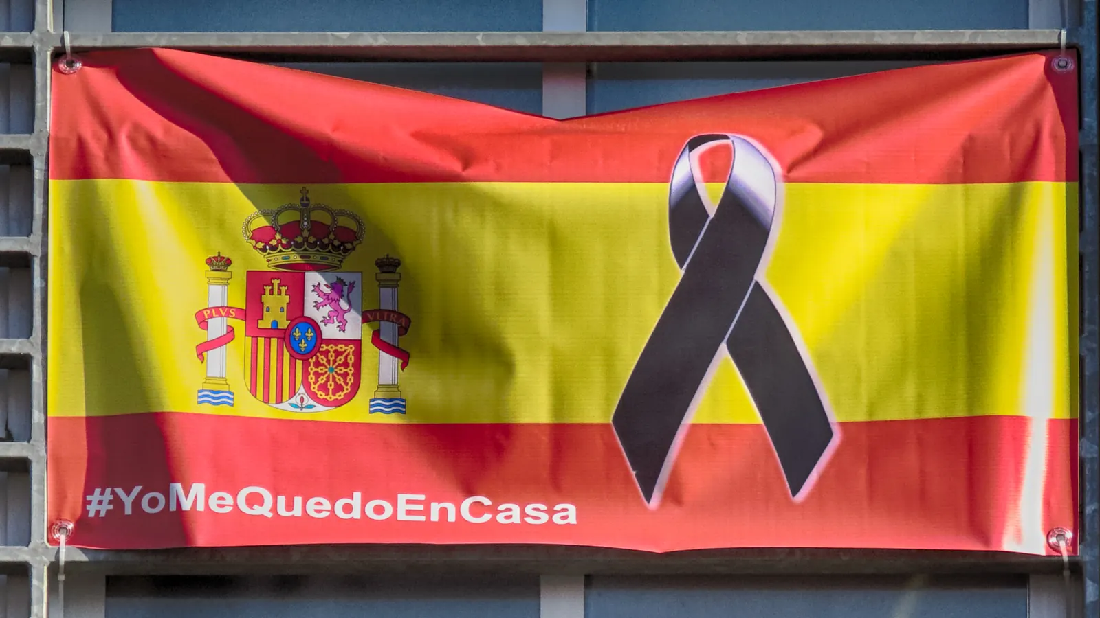 Bandera de España con un lazo negro y el lema #YoMeQuedoEnCasa, colgada en una fachada de Alcalá de Henares en 2020
