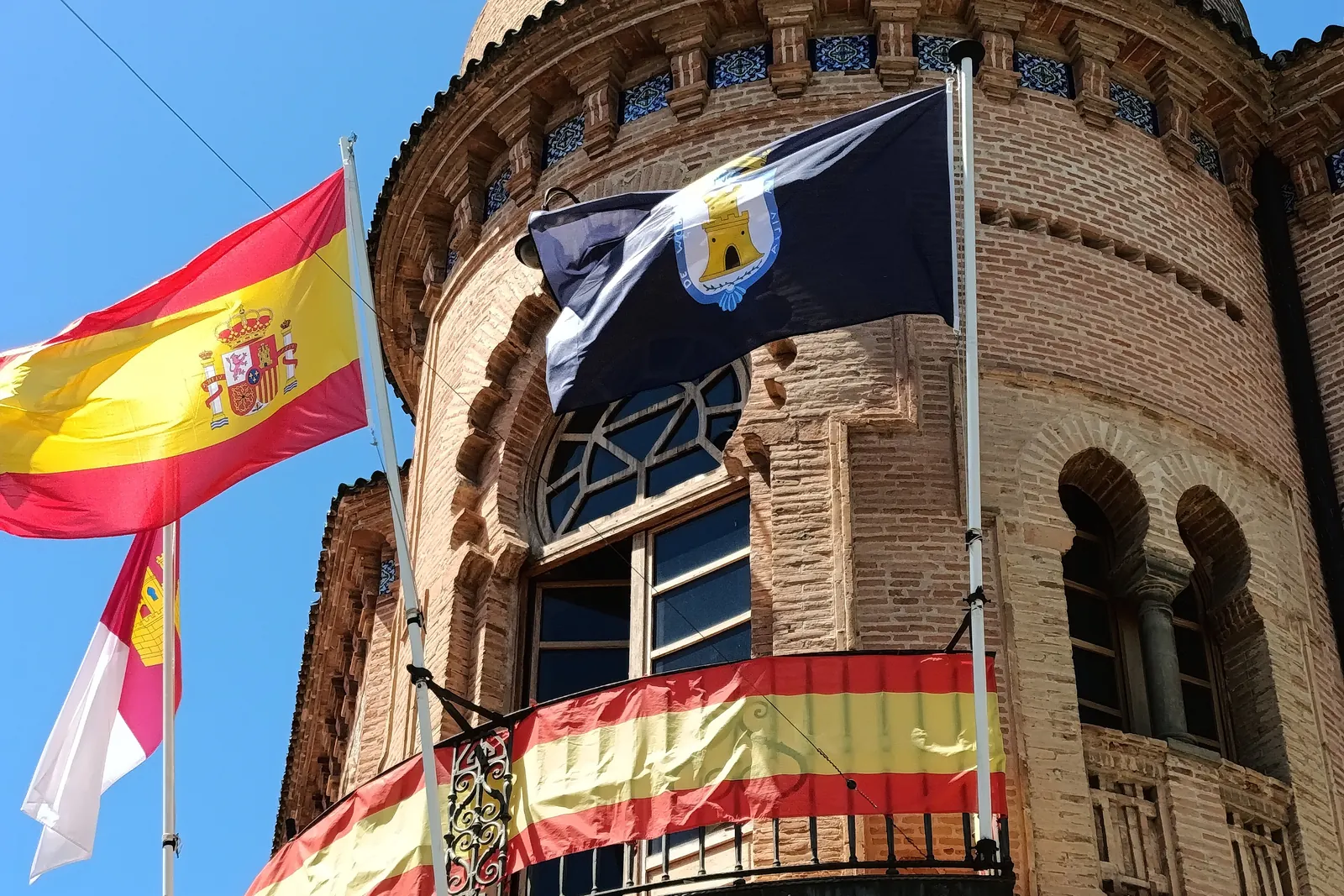 Torre del Ayuntamiento de Mora con la bandera de España, la del municipio y la de Castilla-La Mancha, y colgaduras rojigualdas en el balcón