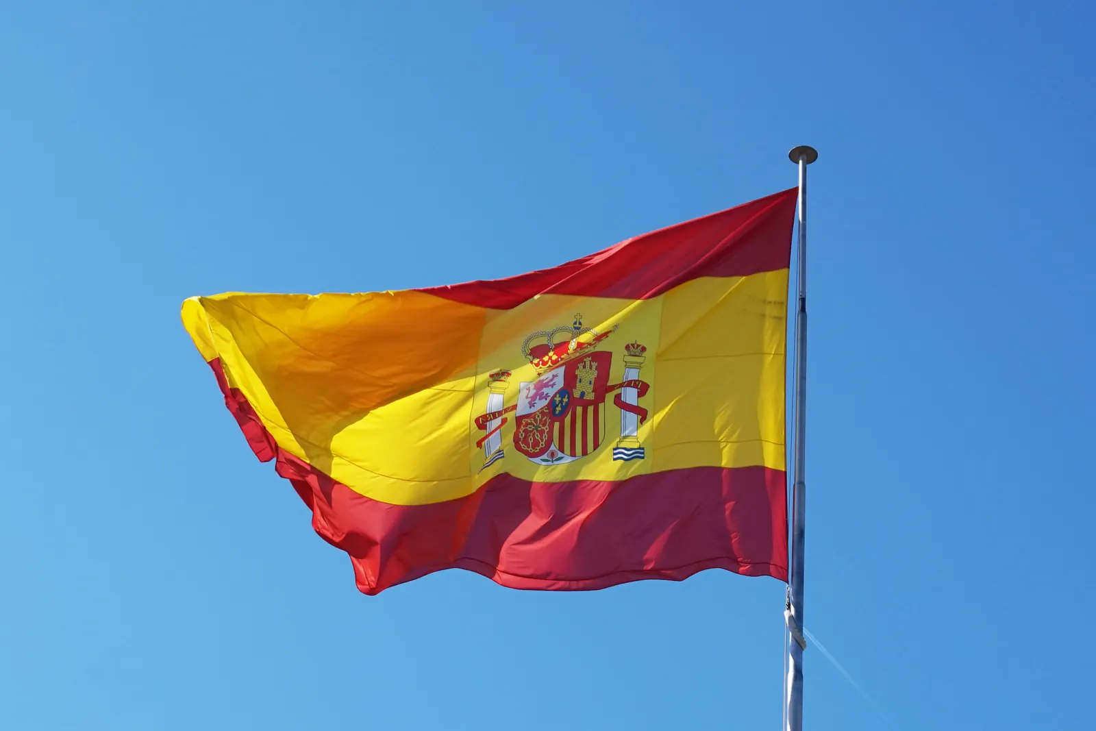 La bandera roja y amarilla con el escudo ondea en un mástil ante un cielo azul en Santander