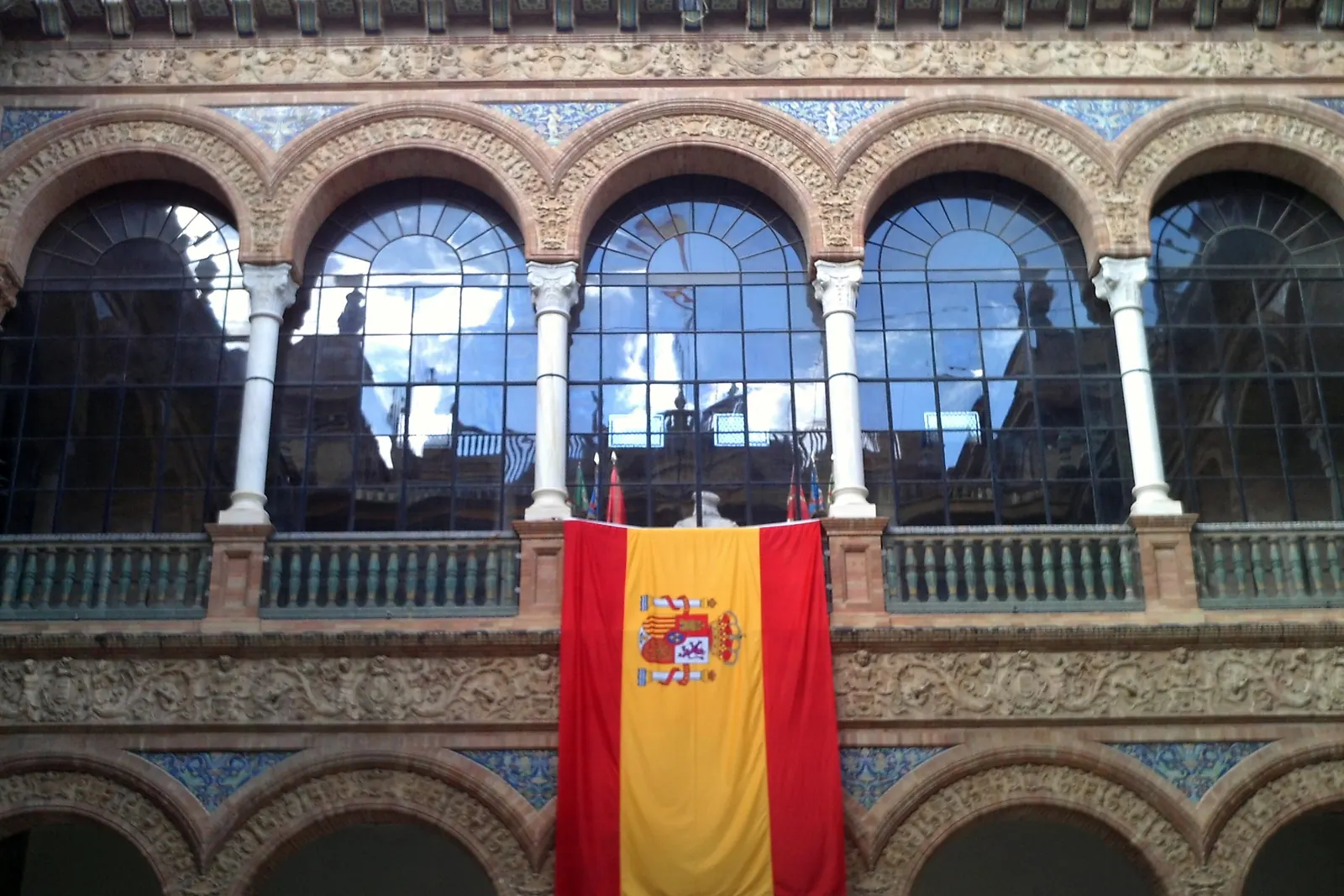 Una bandera de España con escudo cuelga entre los arcos del patio de la Capitanía General de Sevilla