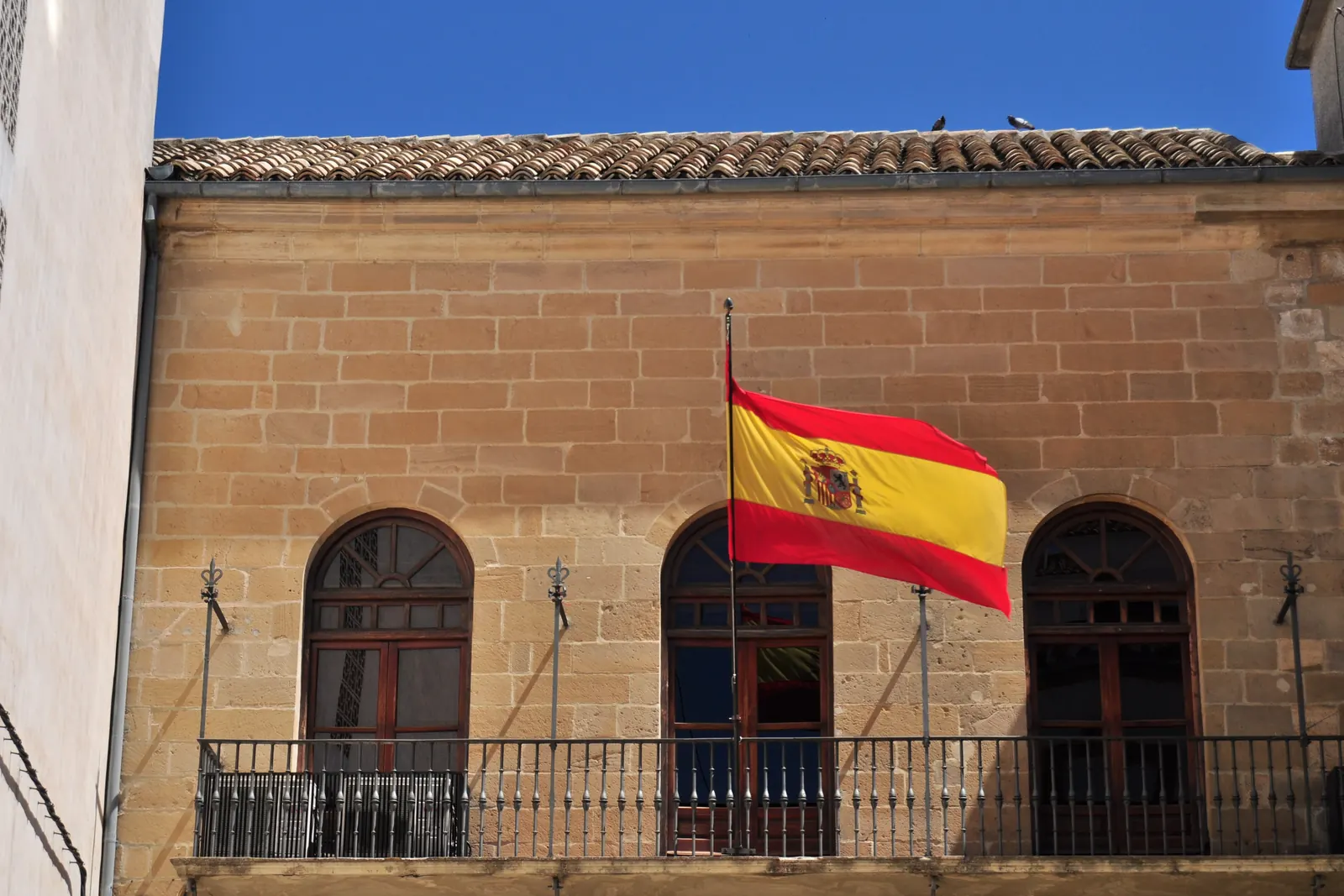 Una bandera de España en un asta de fachada sobre un balcón de piedra en Úbeda
