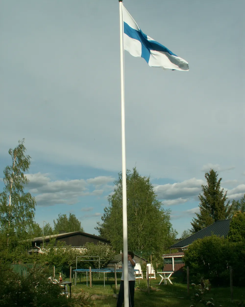 Valkoinen lippusalko ja Suomen lippu omakotitalon pihalla kesällä