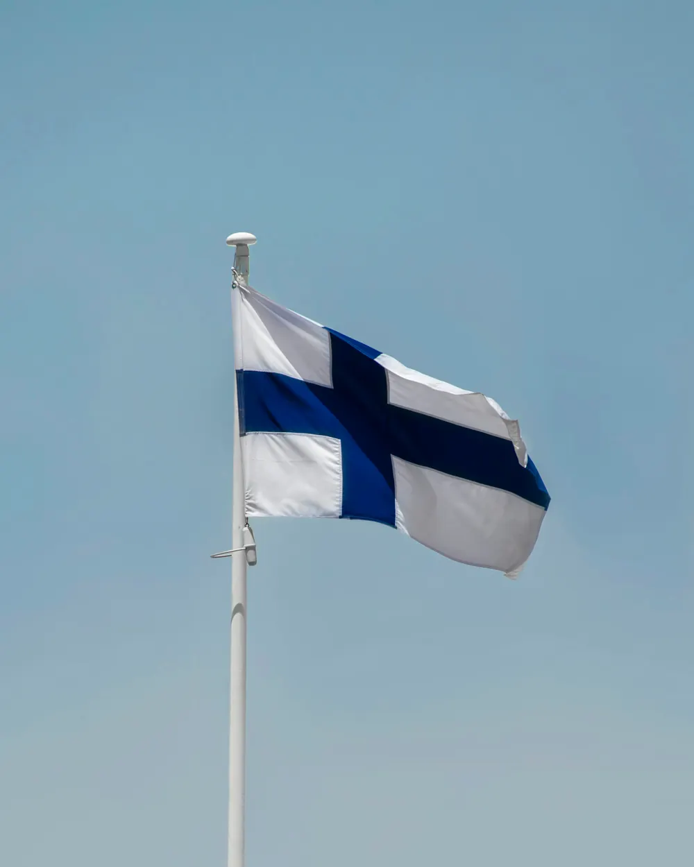 Suomen lippu korkeassa salossa vaaleaa taivasta vasten