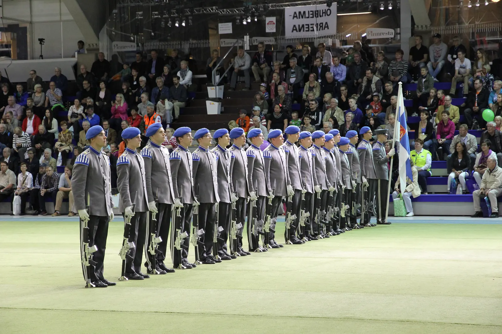 Varusmiessoittokunta rivissä hallissa ja Suomen lippu rivin päässä