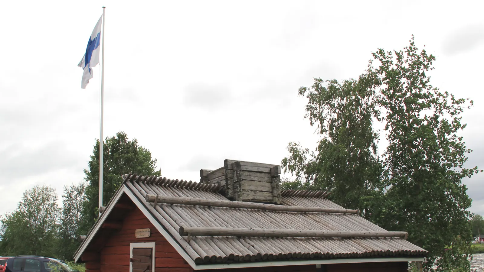 Punainen hirsimaja ja valkoinen lippusalko, jossa on Suomen lippu