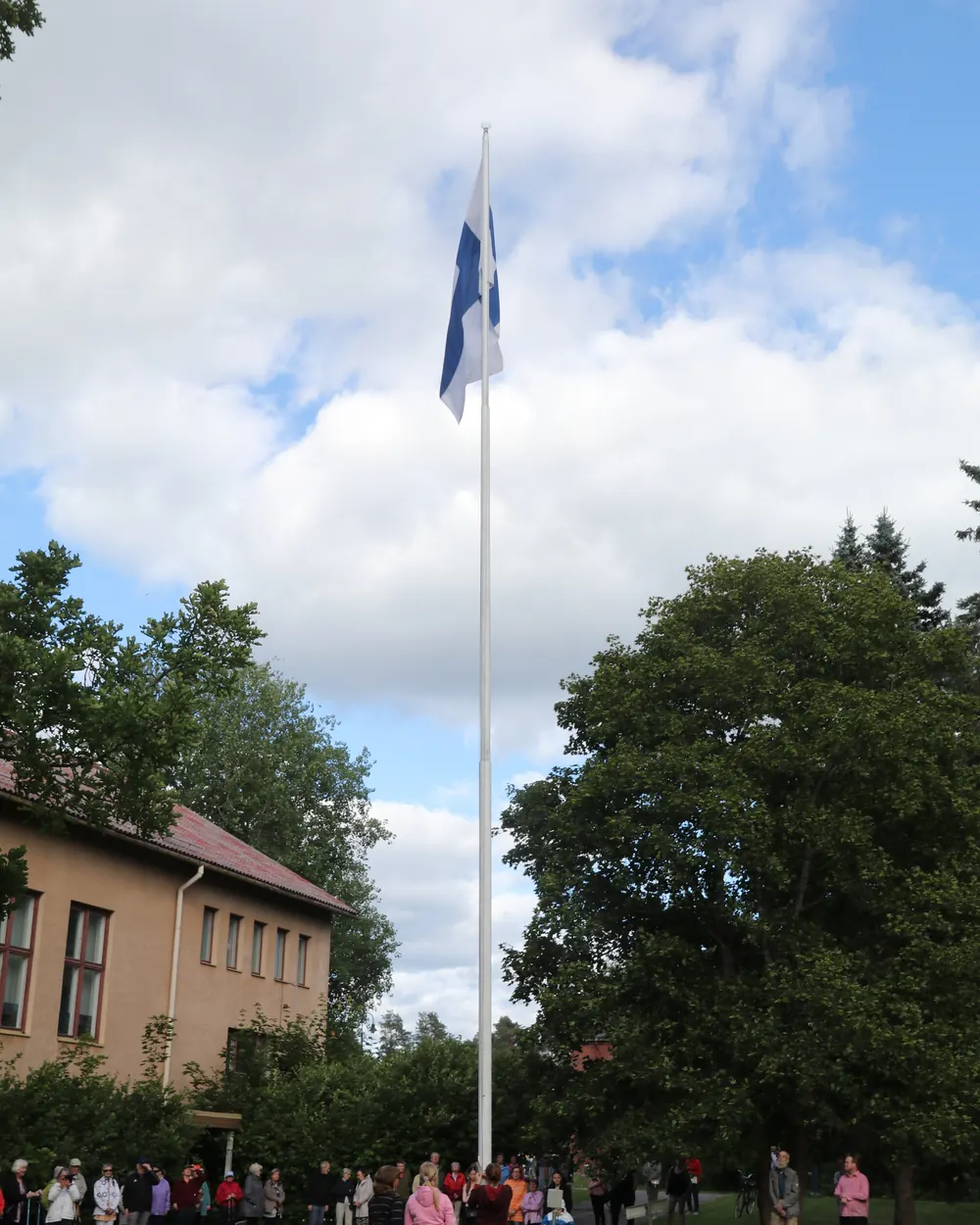 Suomen lippu korkeassa salossa ja ihmisiä kirkon pihalla