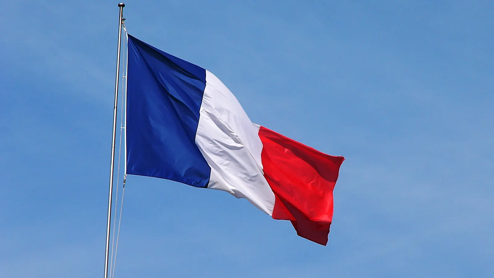 Le drapeau tricolore flotte en haut d’un mât dans un ciel bleu