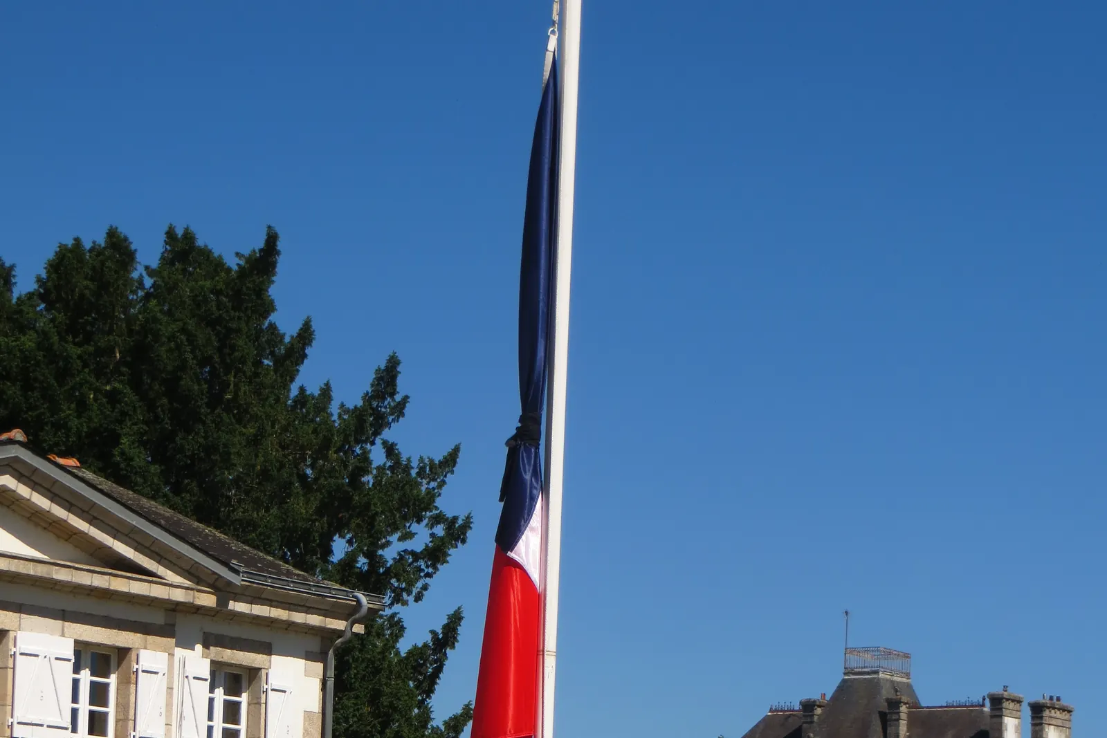 Le drapeau tricolore à mi-hauteur d’un grand mât devant des bâtiments