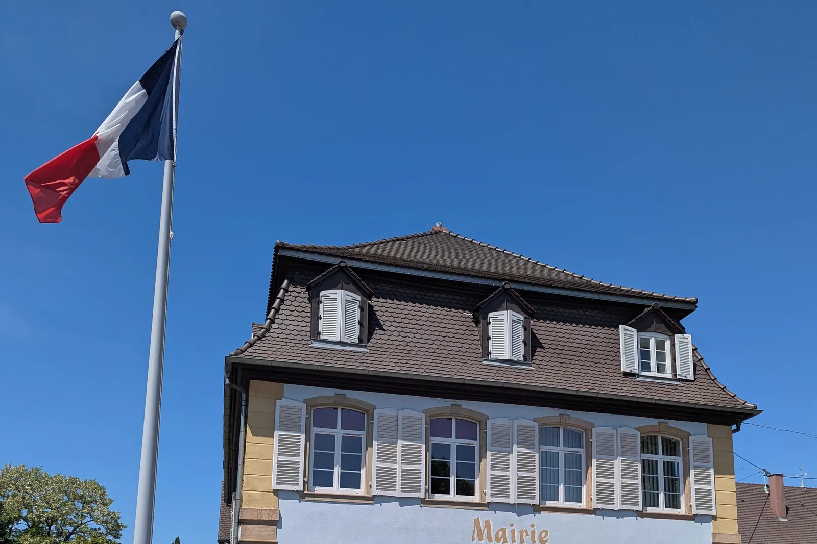 Un mât avec le drapeau tricolore devant la mairie de Rœschwoog