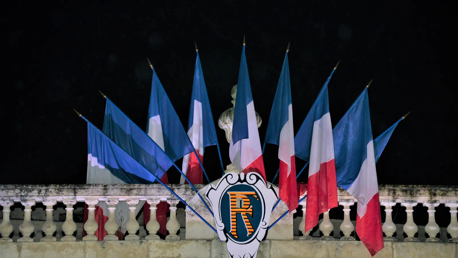 Faisceau de drapeaux tricolores autour d’un écusson RF sur la façade de la préfecture de La Rochelle, la nuit
