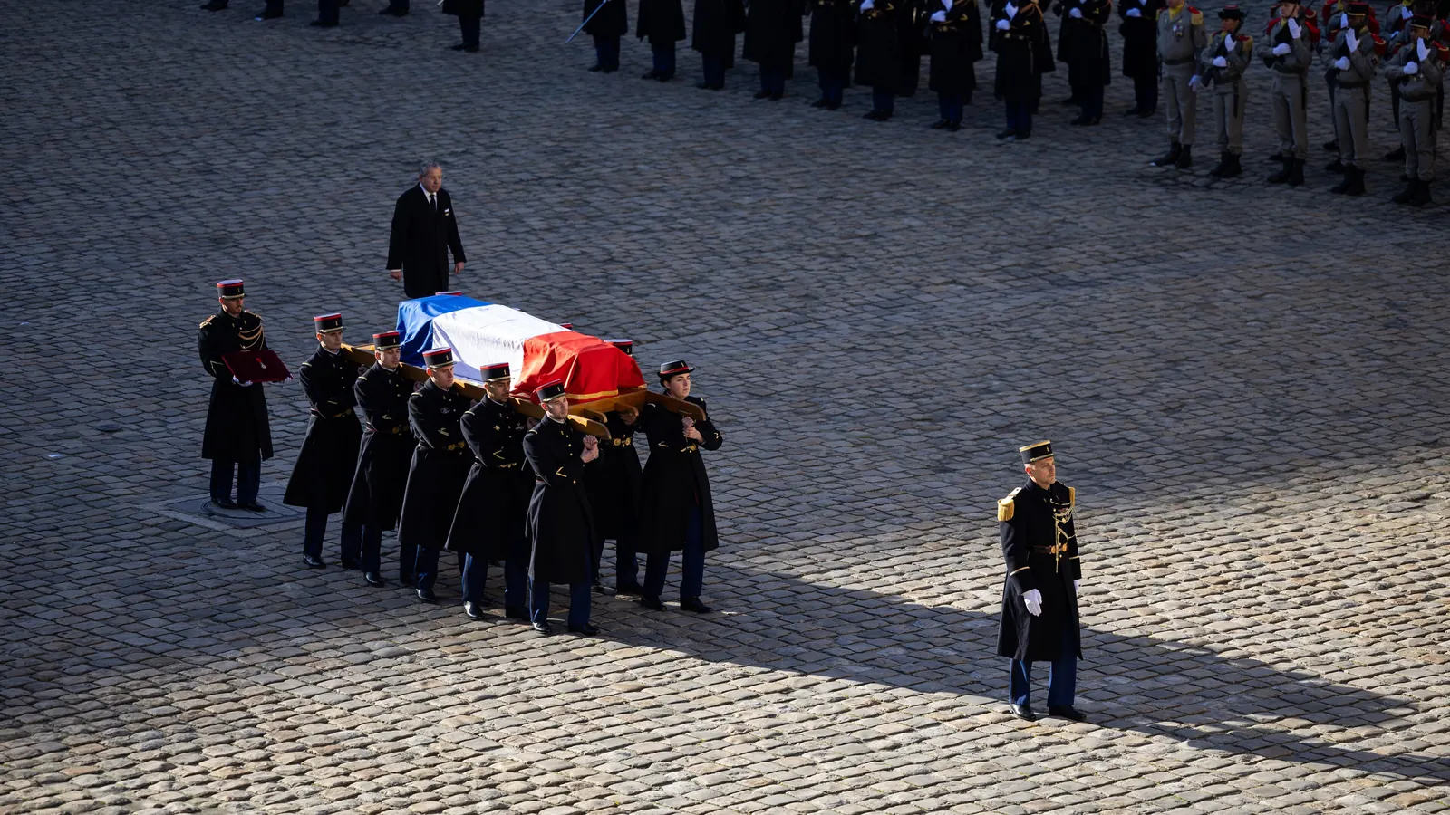 Un cercueil recouvert du drapeau tricolore porté par des gardes républicains dans la cour des Invalides