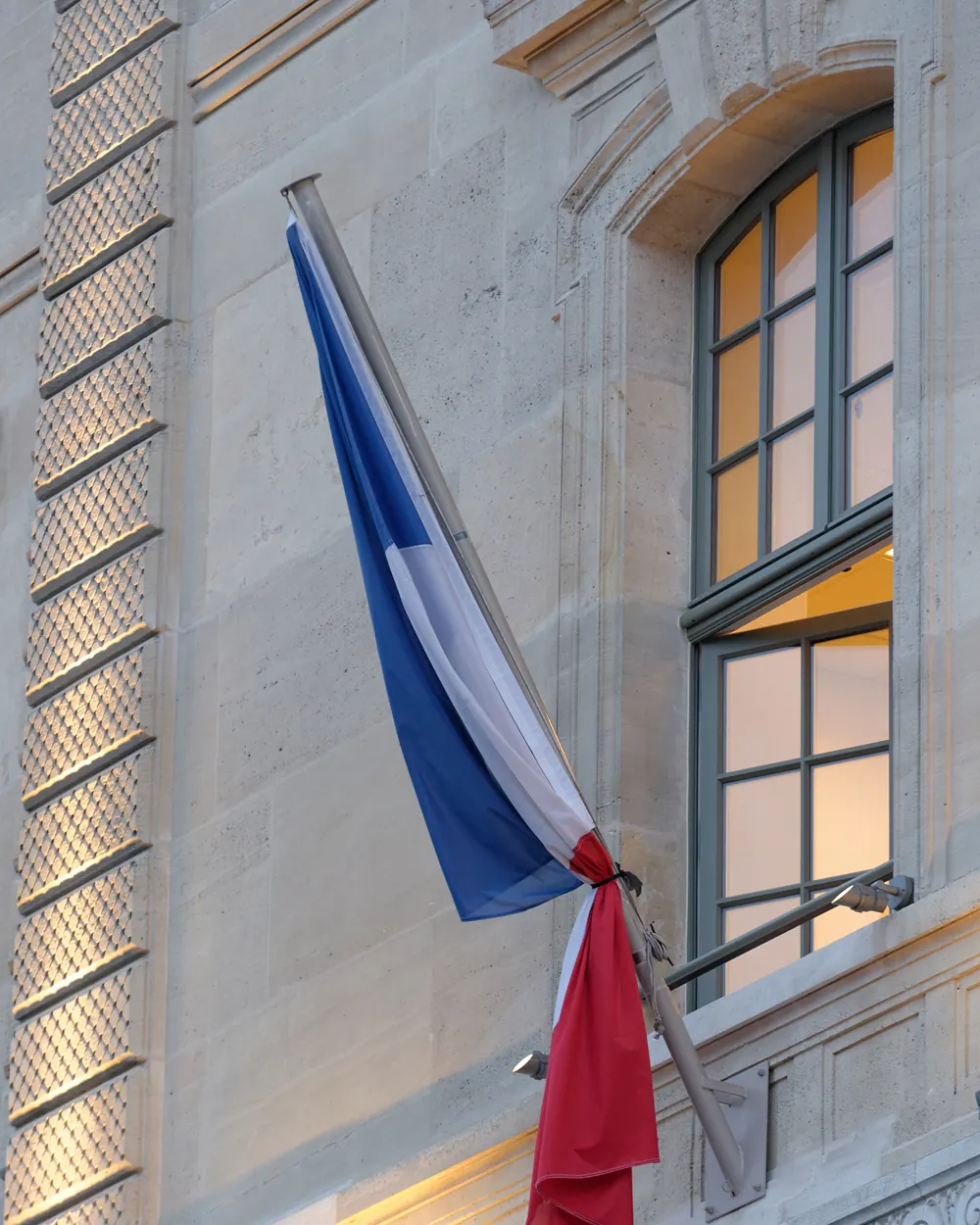 Un drapeau tricolore noué d’un ruban noir à sa hampe sur une façade