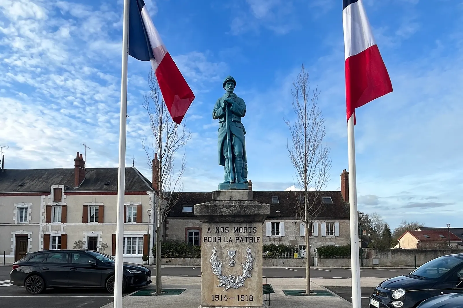 Deux drapeaux tricolores à des mâts de part et d’autre du monument aux morts de Poilly-lez-Gien