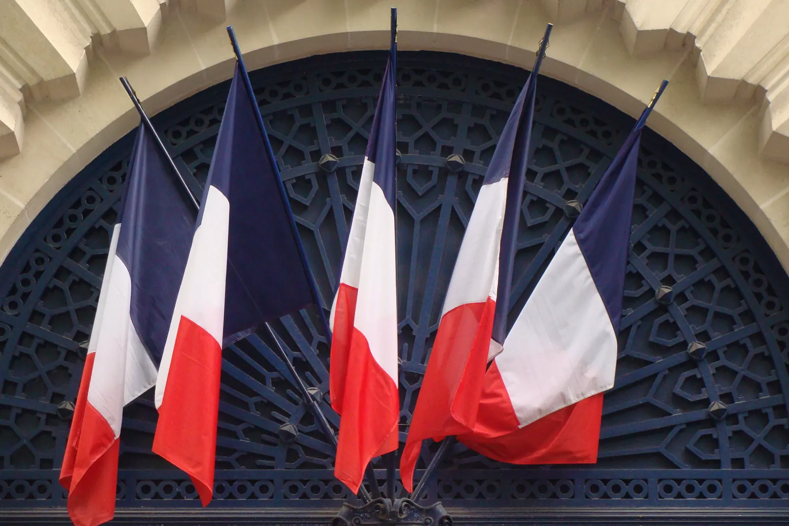 Cinq drapeaux tricolores en éventail devant une grille de la caserne de la Garde républicaine