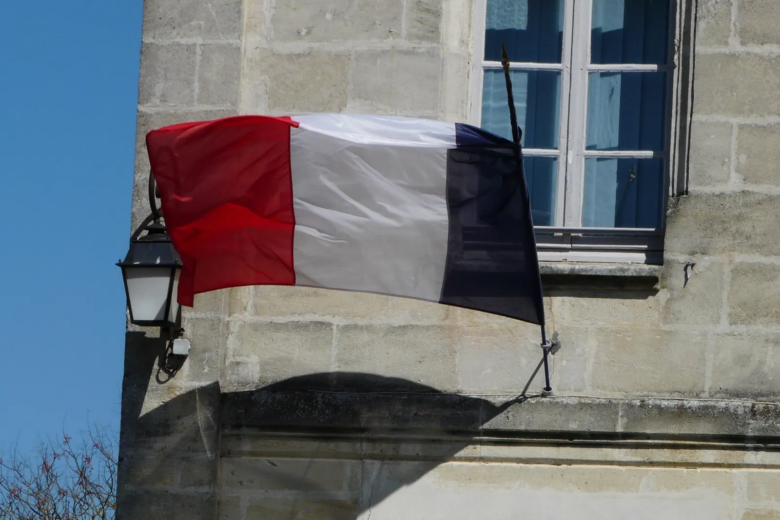 Un drapeau tricolore à une hampe sur la façade en pierre d’une mairie