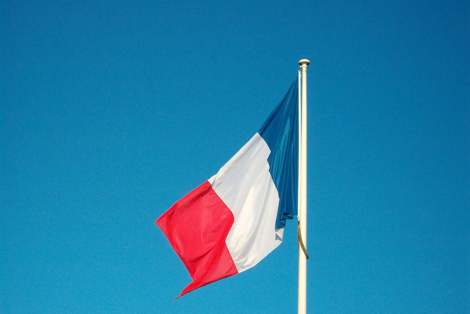 Le drapeau français flotte à un mât blanc devant un ciel bleu