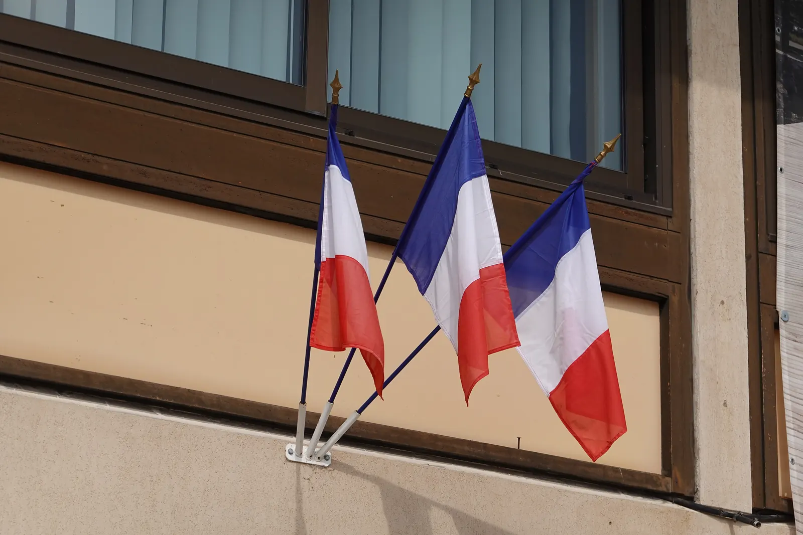 Trois drapeaux tricolores à des hampes fixées dans un support sous une fenêtre