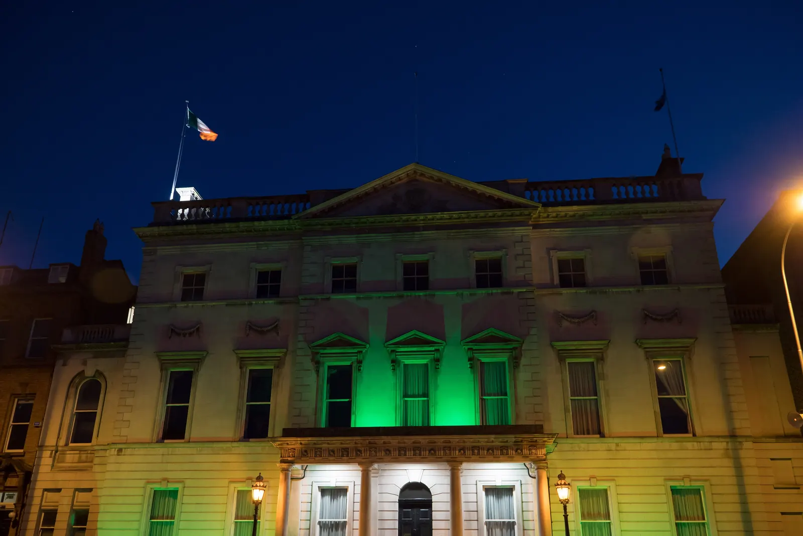 A building lit in green at night with a flag on the roof