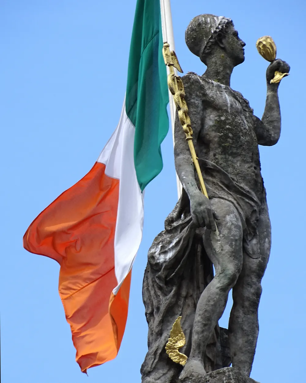The Irish tricolour against a blue sky behind a statue on the General Post Office in Dublin