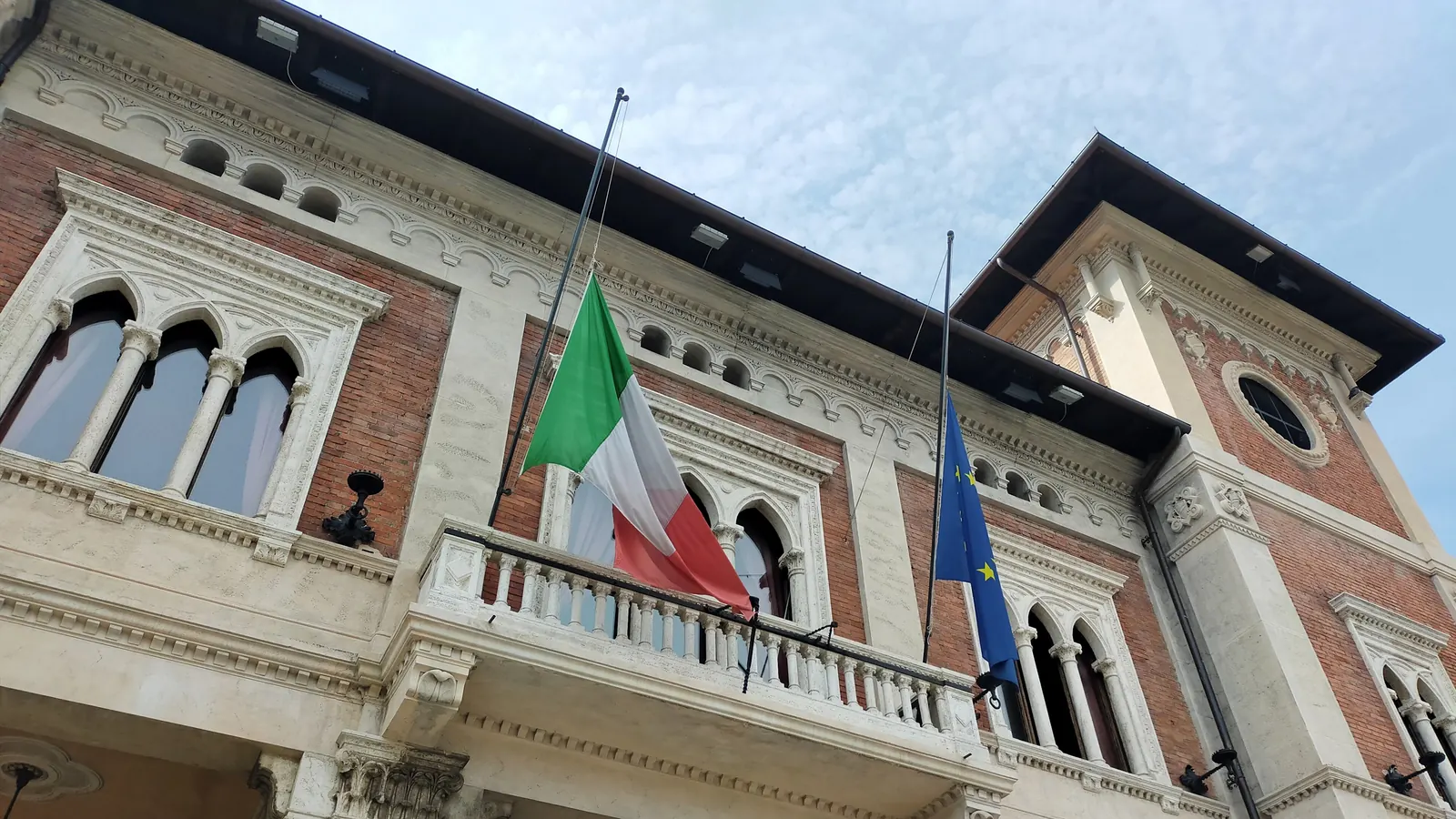 Il Tricolore a mezz'asta sul balcone di un municipio, accanto alla bandiera europea