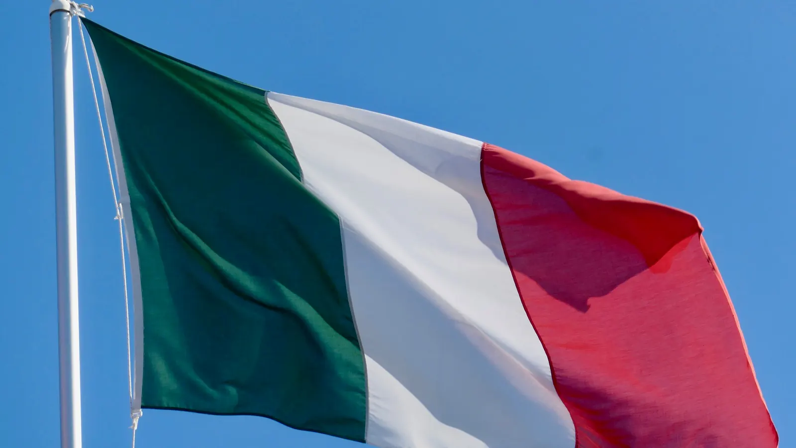 Il Tricolore verde, bianco e rosso spiegato dal vento su un pennone, contro il cielo azzurro