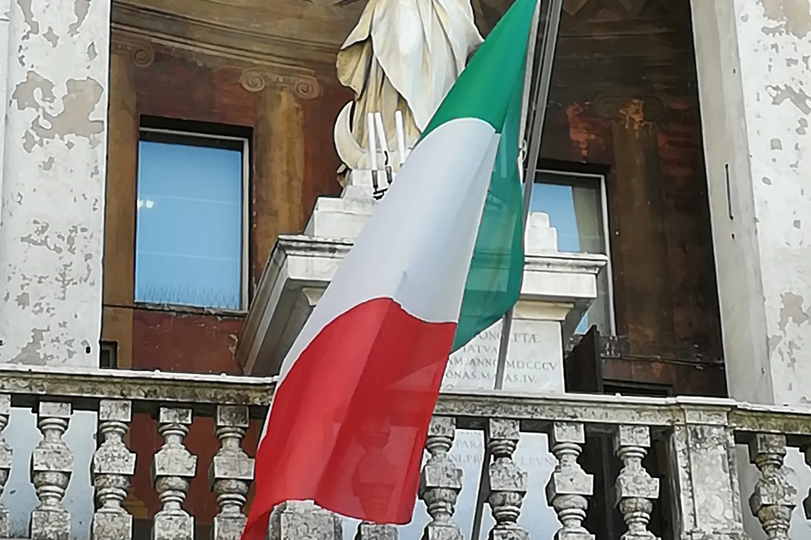 Il Tricolore su un'asta inclinata dal balcone di pietra di un palazzo comunale