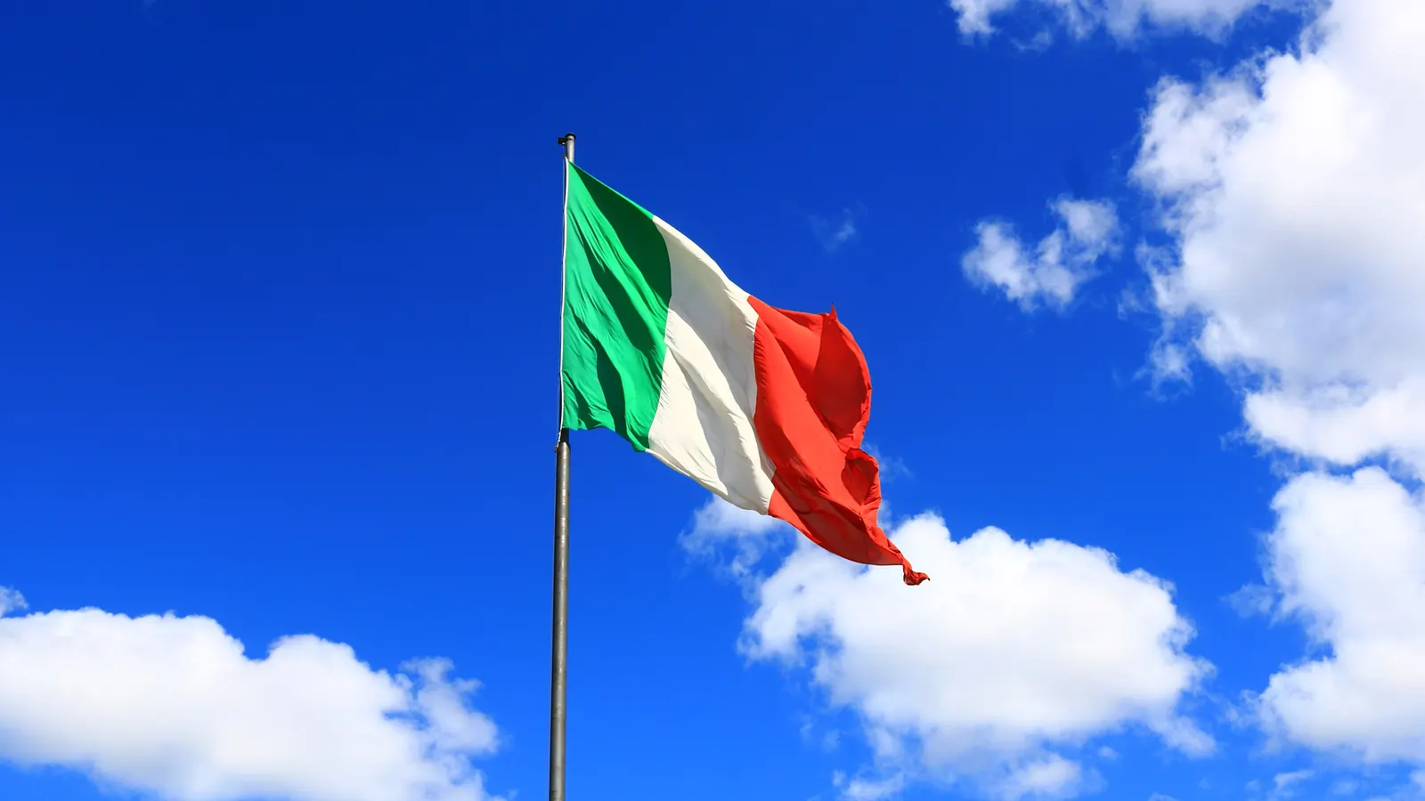 Il Tricolore su un pennone contro un cielo azzurro con nuvole bianche