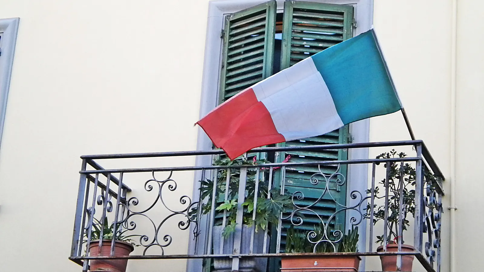 Il Tricolore su un'asta fissata alla ringhiera di un balcone, davanti alle persiane verdi