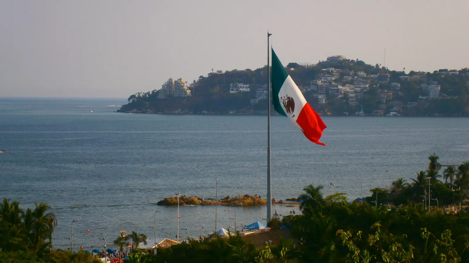 La Bandera Nacional de México en un asta frente a la bahía de Acapulco
