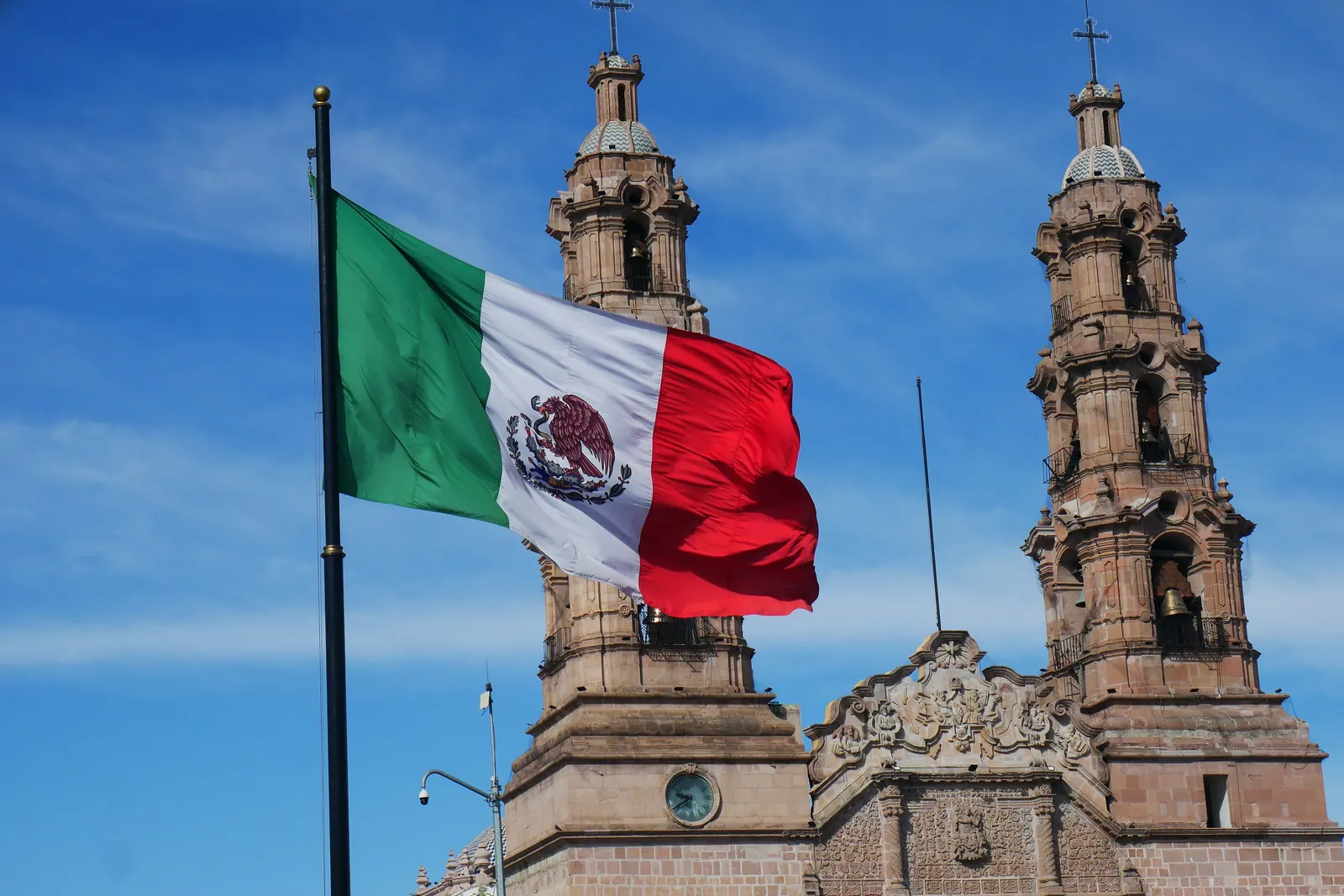 La Bandera Nacional en un asta frente a las torres de la Catedral de Aguascalientes
