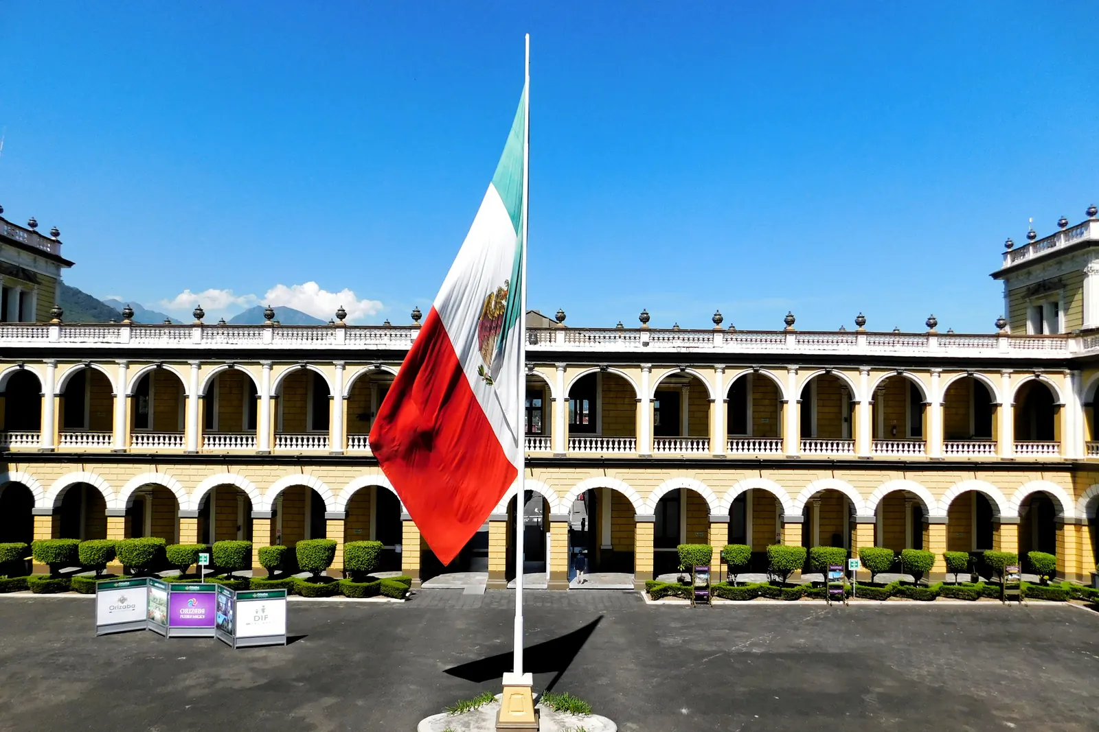 La Bandera Nacional en un asta frente a los arcos de un palacio municipal