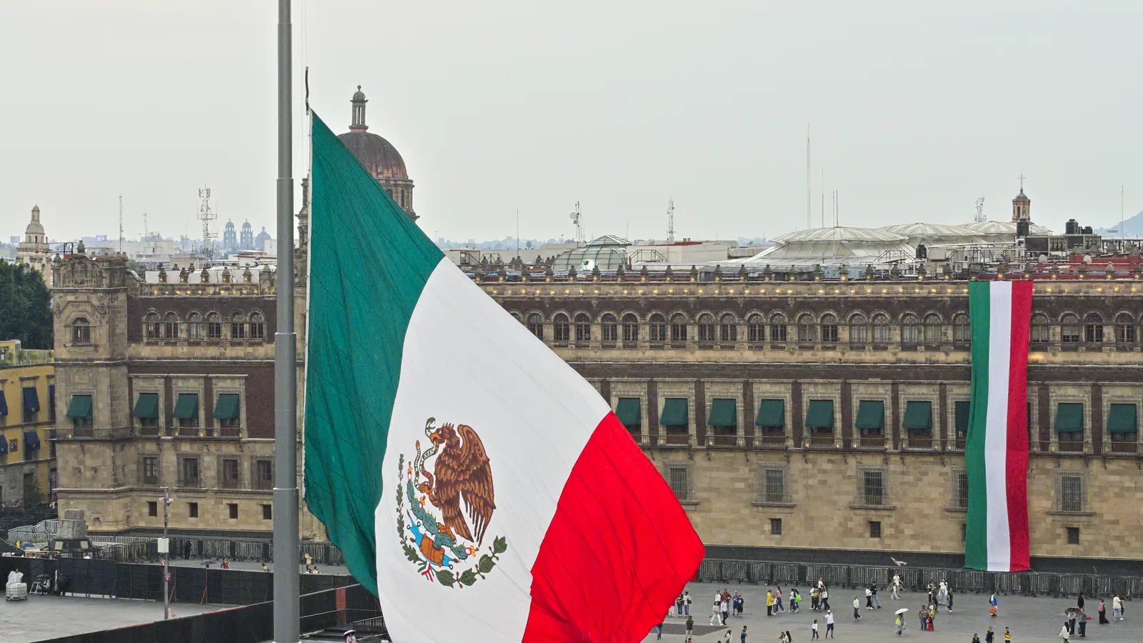 Arriado de la bandera monumental en el Zócalo frente al Palacio Nacional, con el público formando un círculo