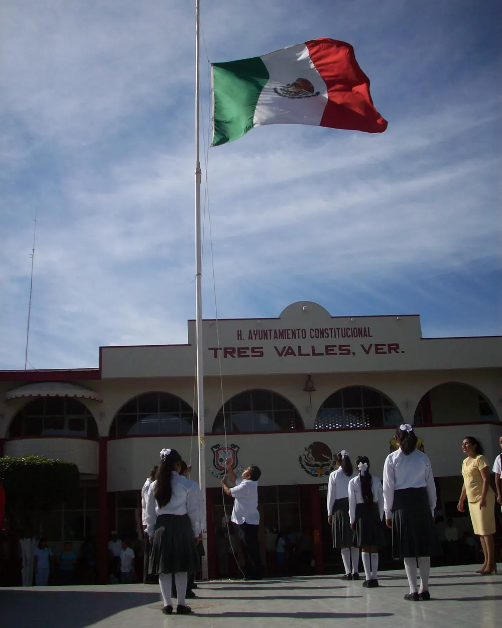 Una escolta escolar rinde honores a la bandera frente a un edificio municipal