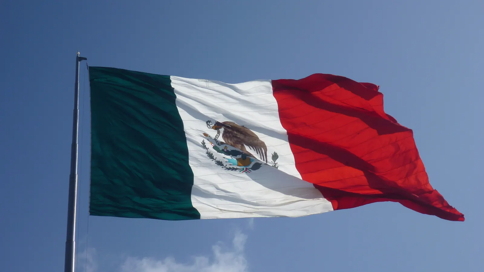La Bandera Nacional tensa por un viento fuerte en un asta, contra un cielo azul