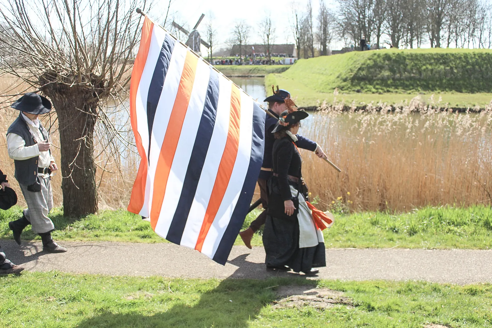 Spelers in historische kleding dragen een grote prinsenvlag in oranje, wit en blauw