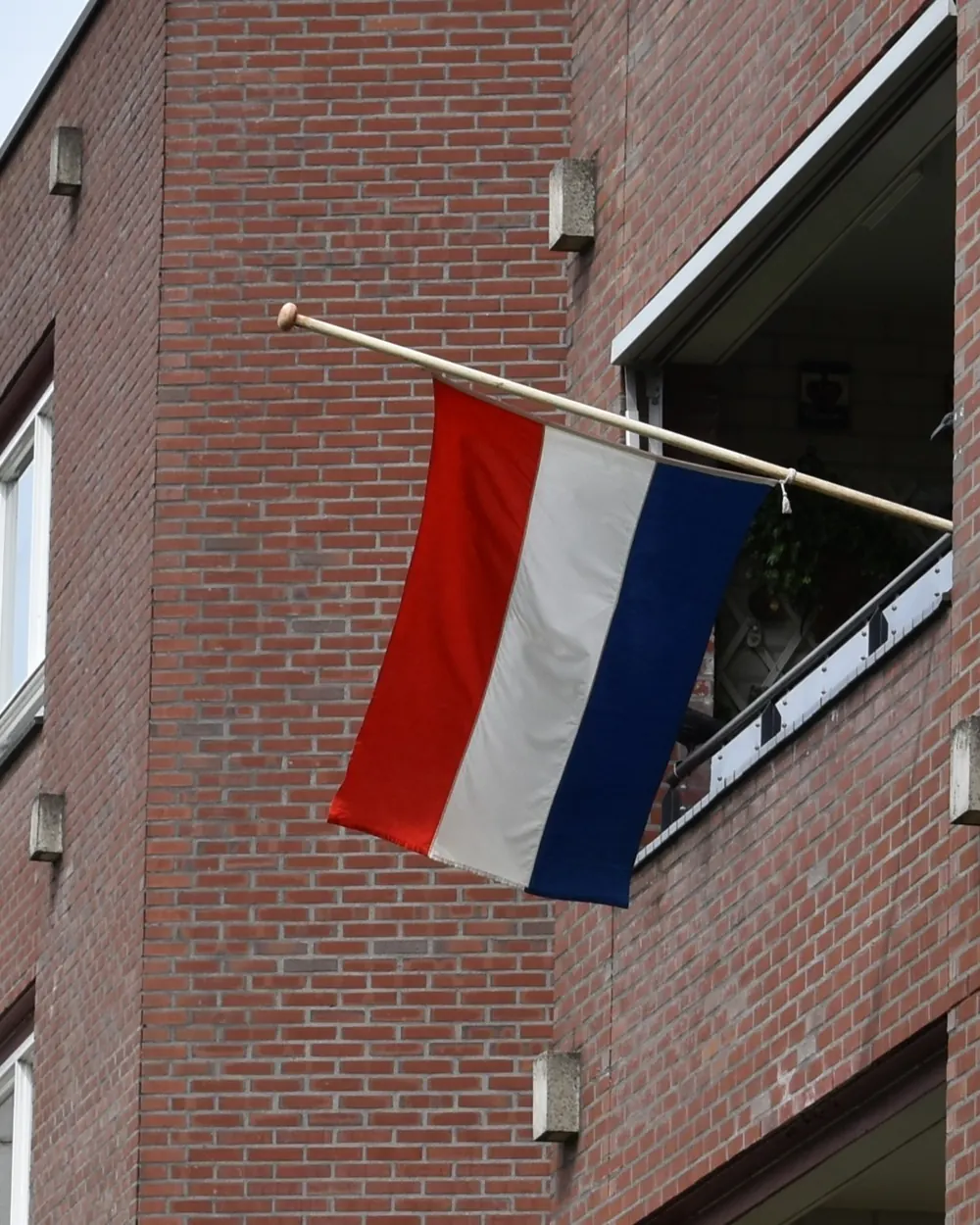 De Nederlandse vlag hangt halfstok aan een stok aan een bakstenen flat