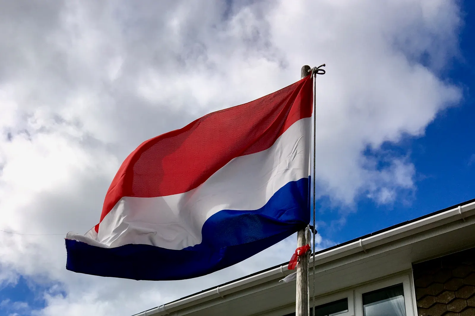 De Nederlandse vlag aan een vrijstaande mast naast een woonhuis