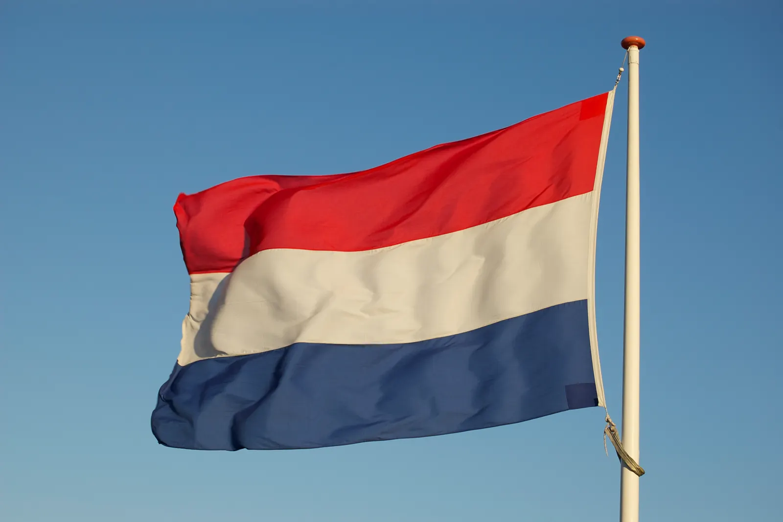 De Nederlandse vlag waait aan een mast tegen een blauwe lucht