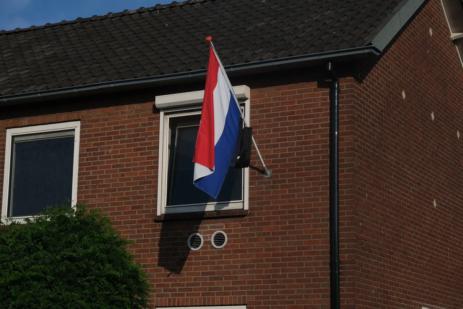 De Nederlandse vlag met een schooltas aan een stok aan de gevel van een bakstenen huis