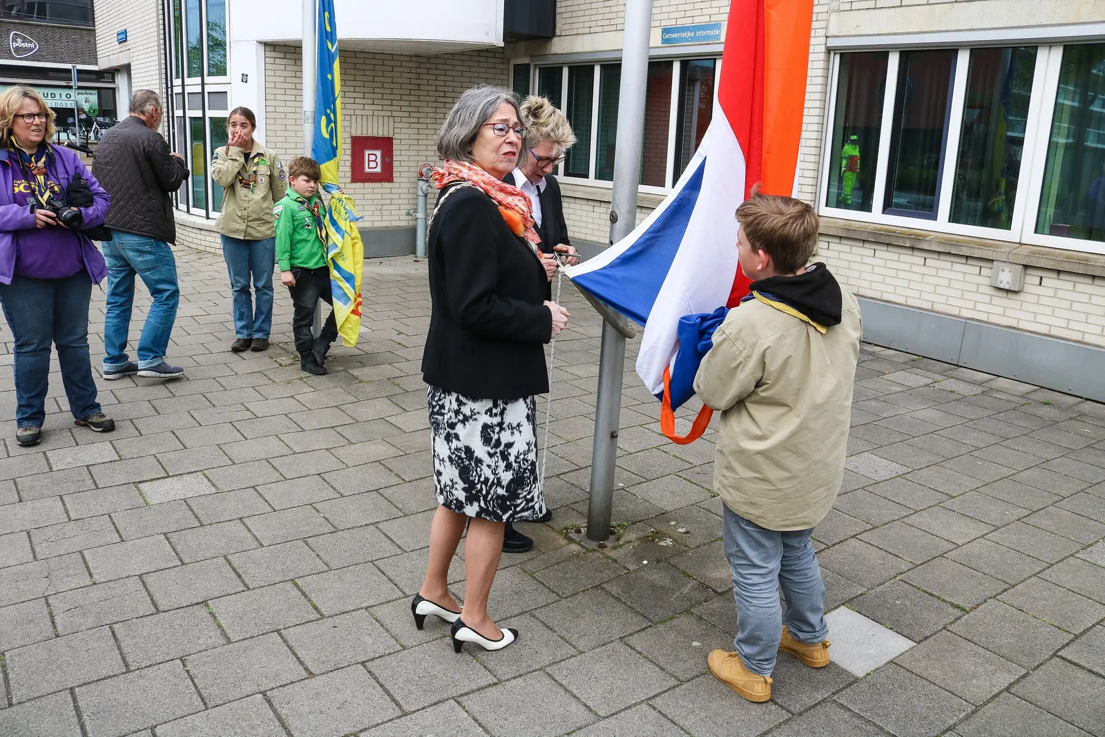 Een vrouw en een jongen hijsen samen de Nederlandse vlag met oranje wimpel