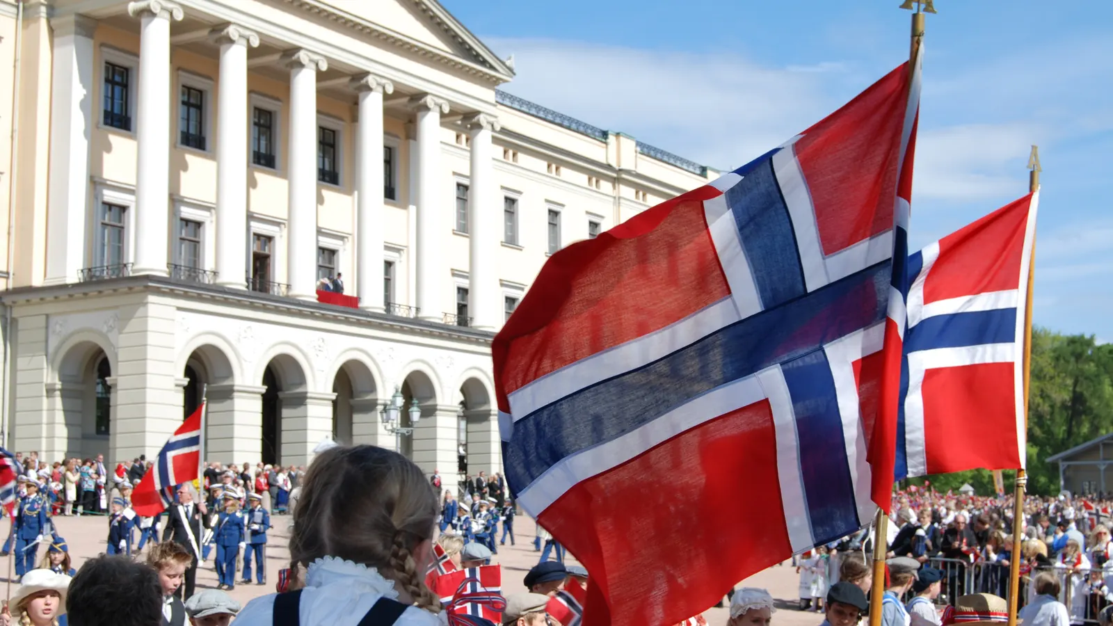Barnetoget med store norske flagg foran Slottet i Oslo på 17. mai