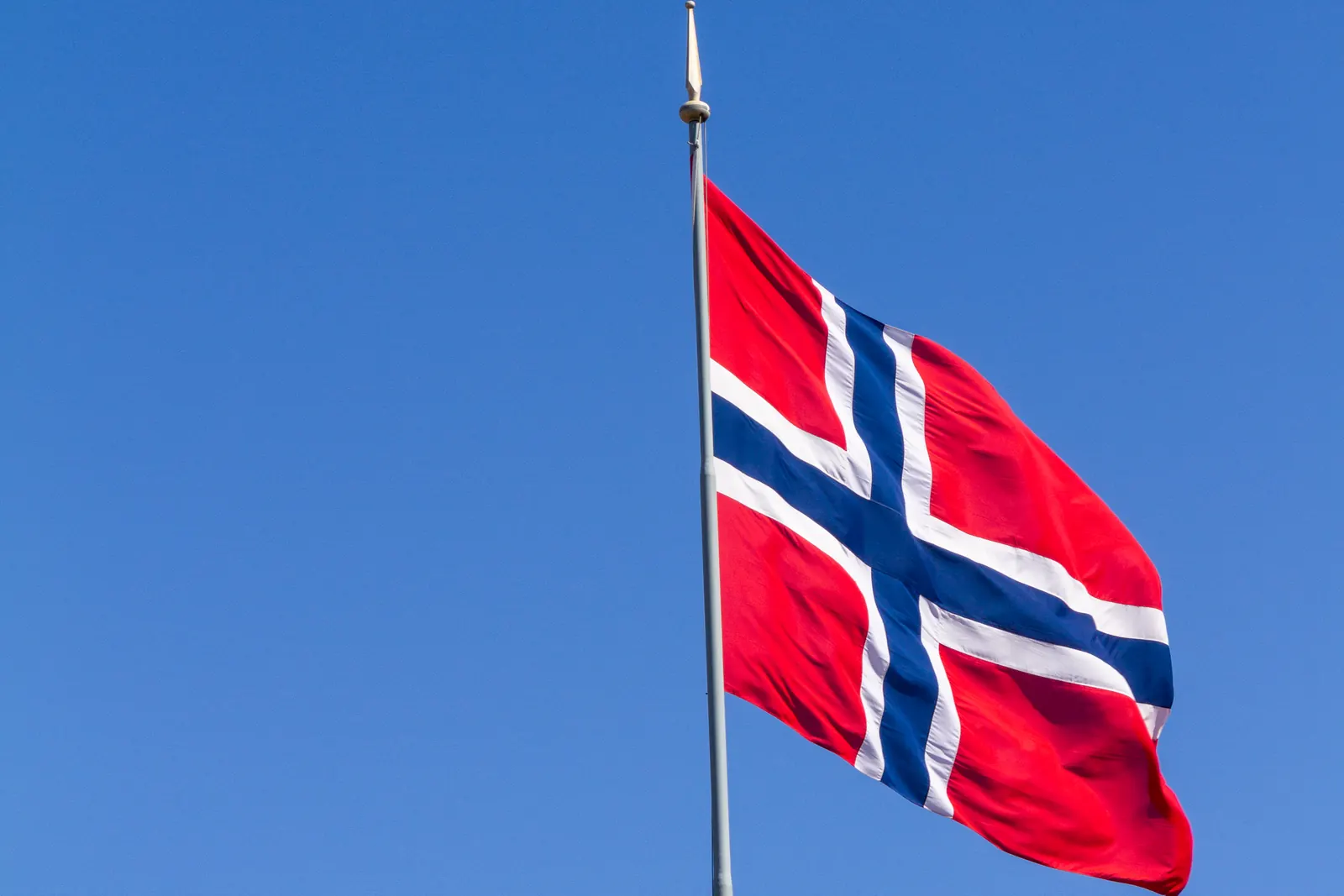 Norsk flagg på en høy stang mot blå himmel i Bergen