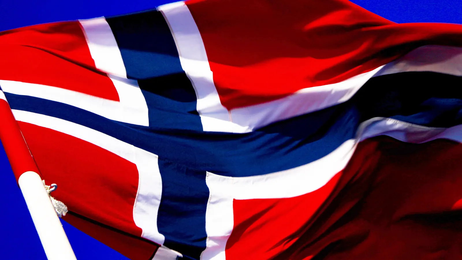 Det norske flagget med rødt felt og blått kors med hvit kant i vinden mot blå himmel