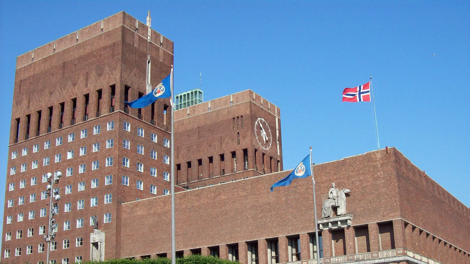 Oslo rådhus med Norges flagg og Oslos byflagg på stengene ved tårnene